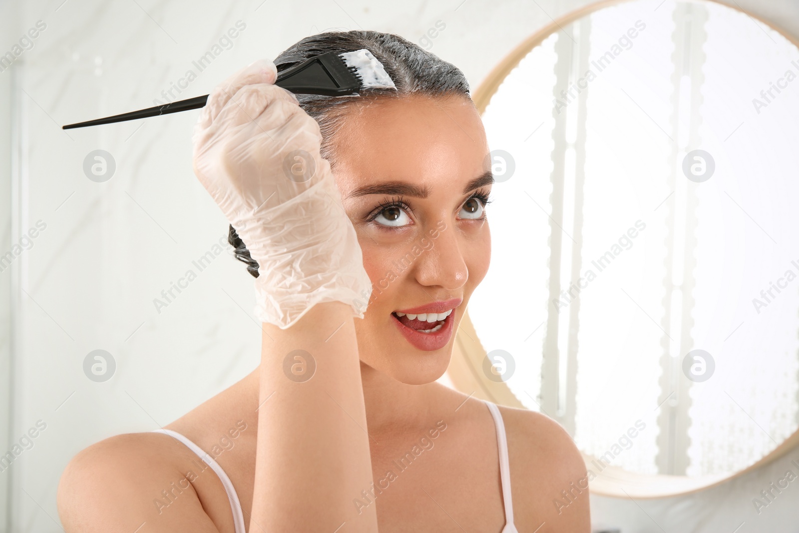 Photo of Young woman dyeing her hair at home