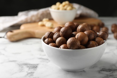 Photo of Bowl with organic Macadamia nuts on marble table. Space for text