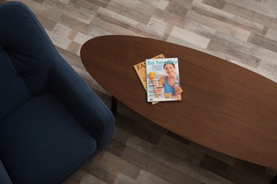 Photo of Magazines on wooden table near armchair indoors, top view