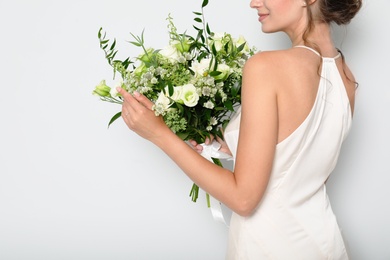 Young bride wearing wedding dress with beautiful bouquet on light grey background, closeup