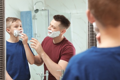 Photo of Dad teaching his son to apply shaving foam on face at mirror