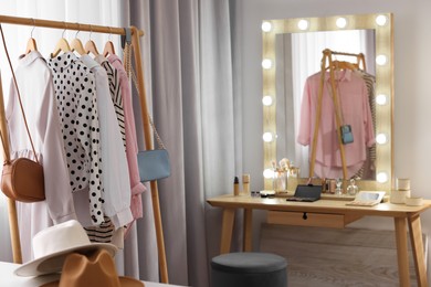 Makeup room. Clothes rack and stylish mirror with light bulbs on dressing table indoors