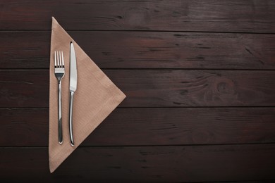 Photo of Fork, knife and napkin on wooden table, top view with space for text. Stylish shiny cutlery set