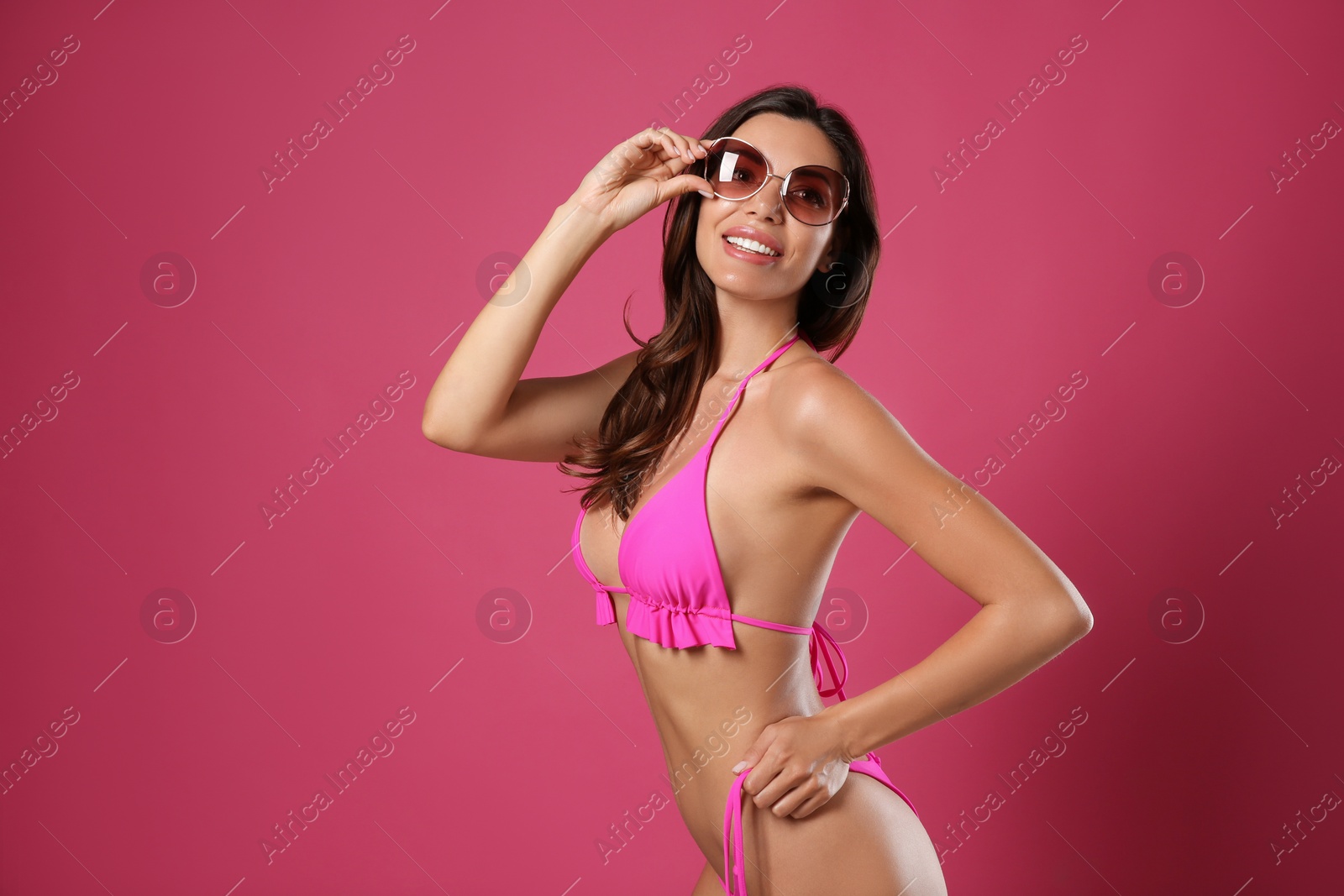 Photo of Beautiful woman in stylish bikini and sunglasses on crimson background