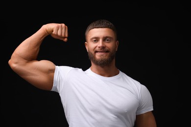 Photo of Young bodybuilder showing his muscular arm on black background
