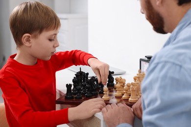 Photo of Father and son playing chess at table indoors, closeup