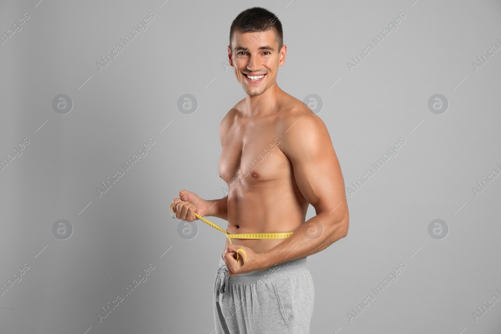 Photo of Young man with slim body using measuring tape on grey background