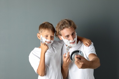 Photo of Father and son shaving together on color background