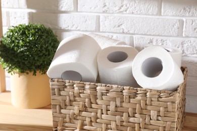 Photo of Toilet paper rolls in wicker basket and floral decor on wooden shelf near white brick wall