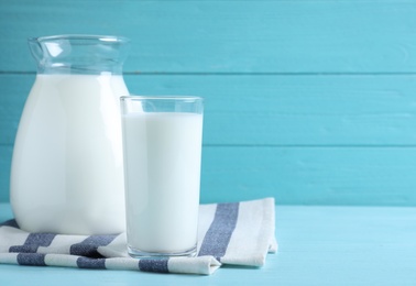 Photo of Jug and glass with fresh milk on light blue wooden table. Space for text