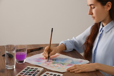 Woman painting flowers with watercolor at wooden table indoors. Creative artwork