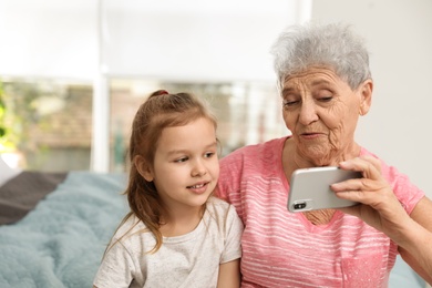 Photo of Cute girl and her grandmother taking selfie  at home