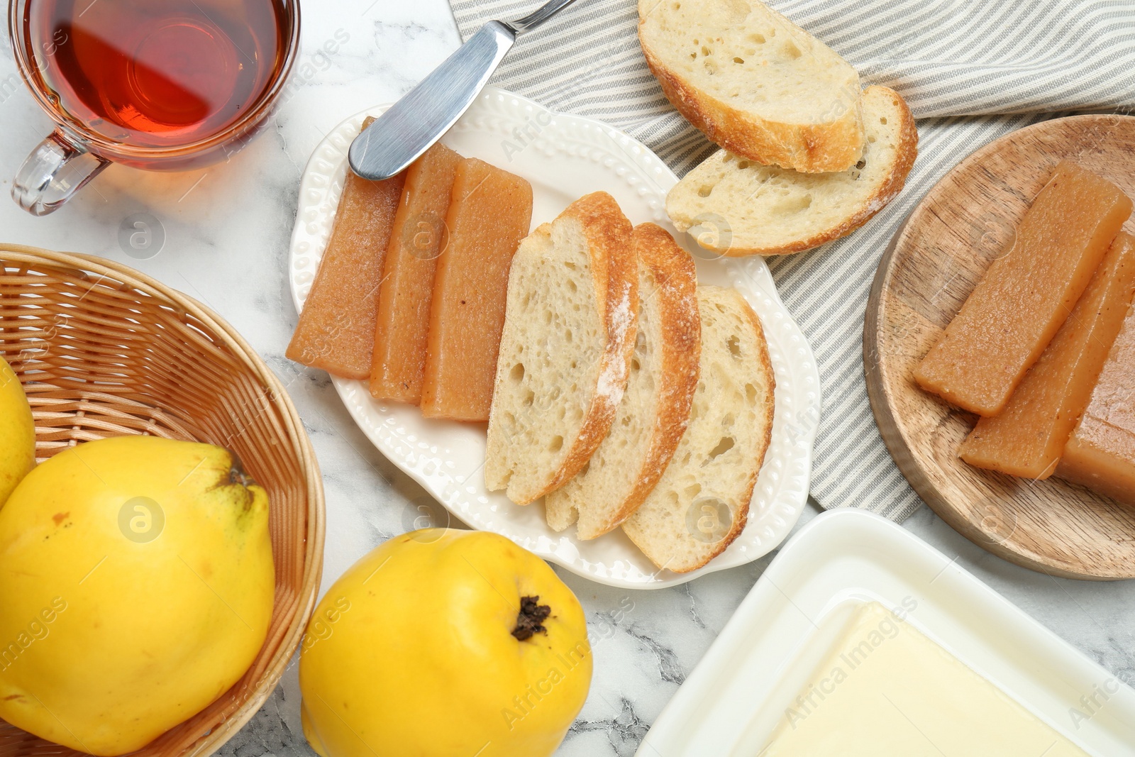 Photo of Delicious quince paste, bread, butter, cup of tea and fresh fruits on white marble table, flat lay