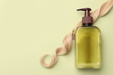 Photo of Lock of hair and shampoo bottle on olive background, flat lay. Space for text