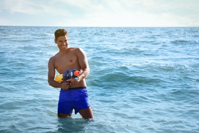Man with water gun having fun in sea. Space for text