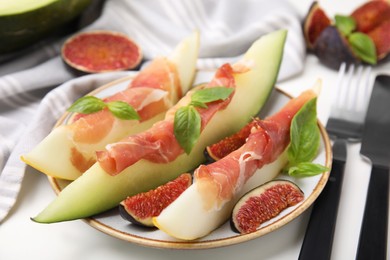 Photo of Tasty melon, jamon and figs served on white table, closeup