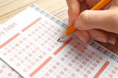 Woman filling out lottery tickets with pencil on wooden table, closeup. Space for text