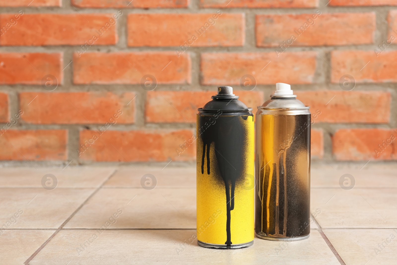 Photo of Used cans of spray paint on floor against brick wall. Space for text