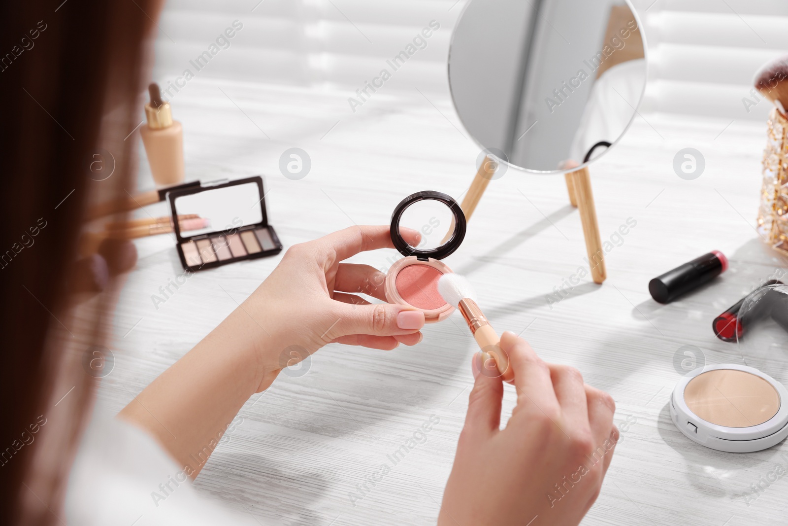 Photo of Woman with blusher and brush at dressing table indoors, closeup