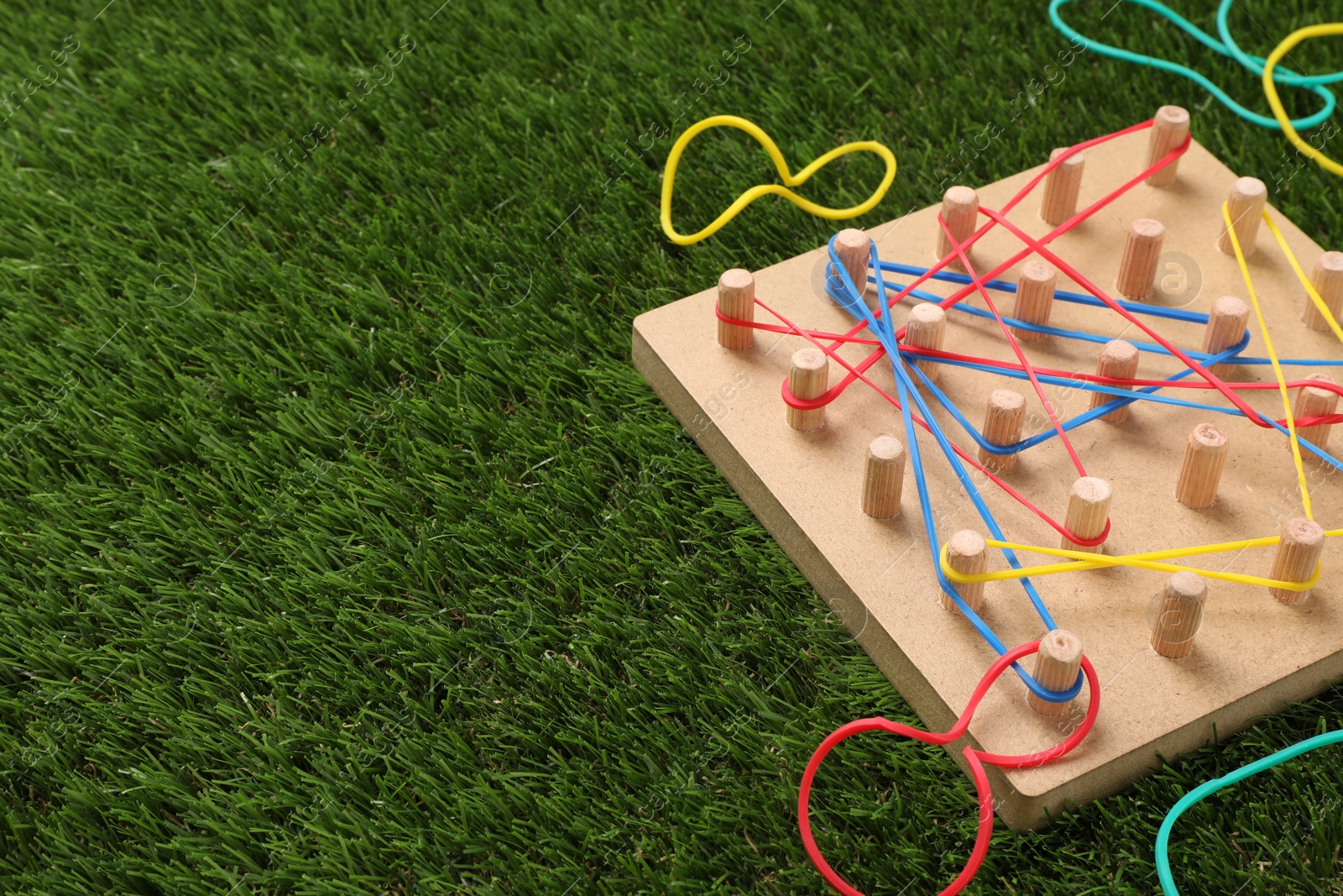 Photo of Wooden geoboard with rubber bands on artificial grass, space for text. Educational toy for motor skills development