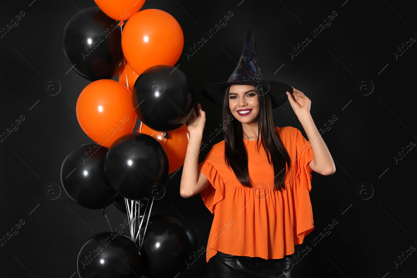 Photo of Beautiful woman wearing witch costume with balloons for Halloween party on black background