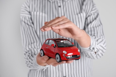 Insurance agent covering toy car on grey background, closeup