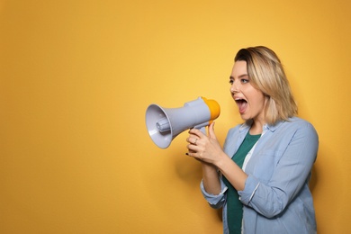 Portrait of emotional woman using megaphone on color background. Space for text