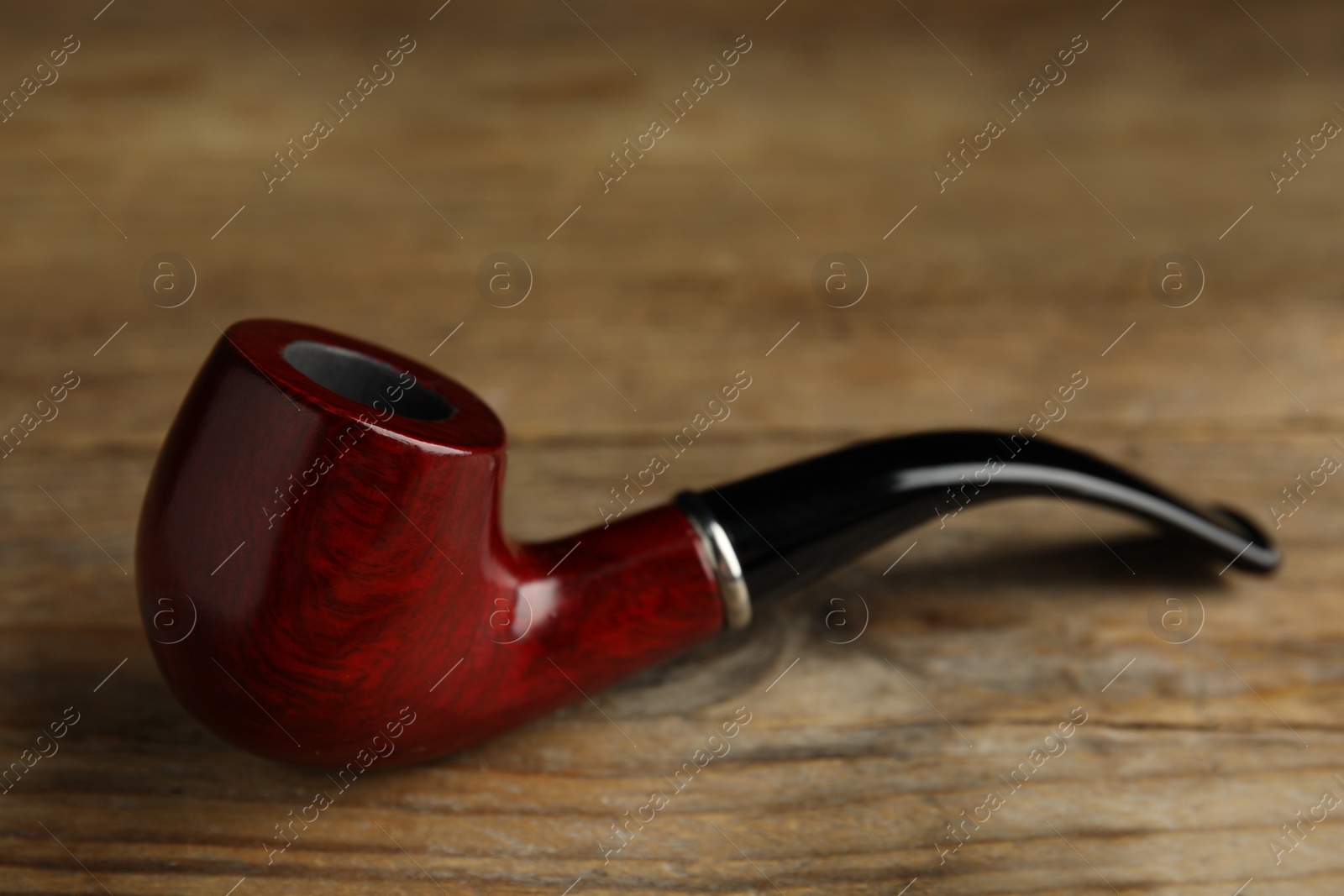 Photo of Classic stylish smoking pipe on wooden table, closeup