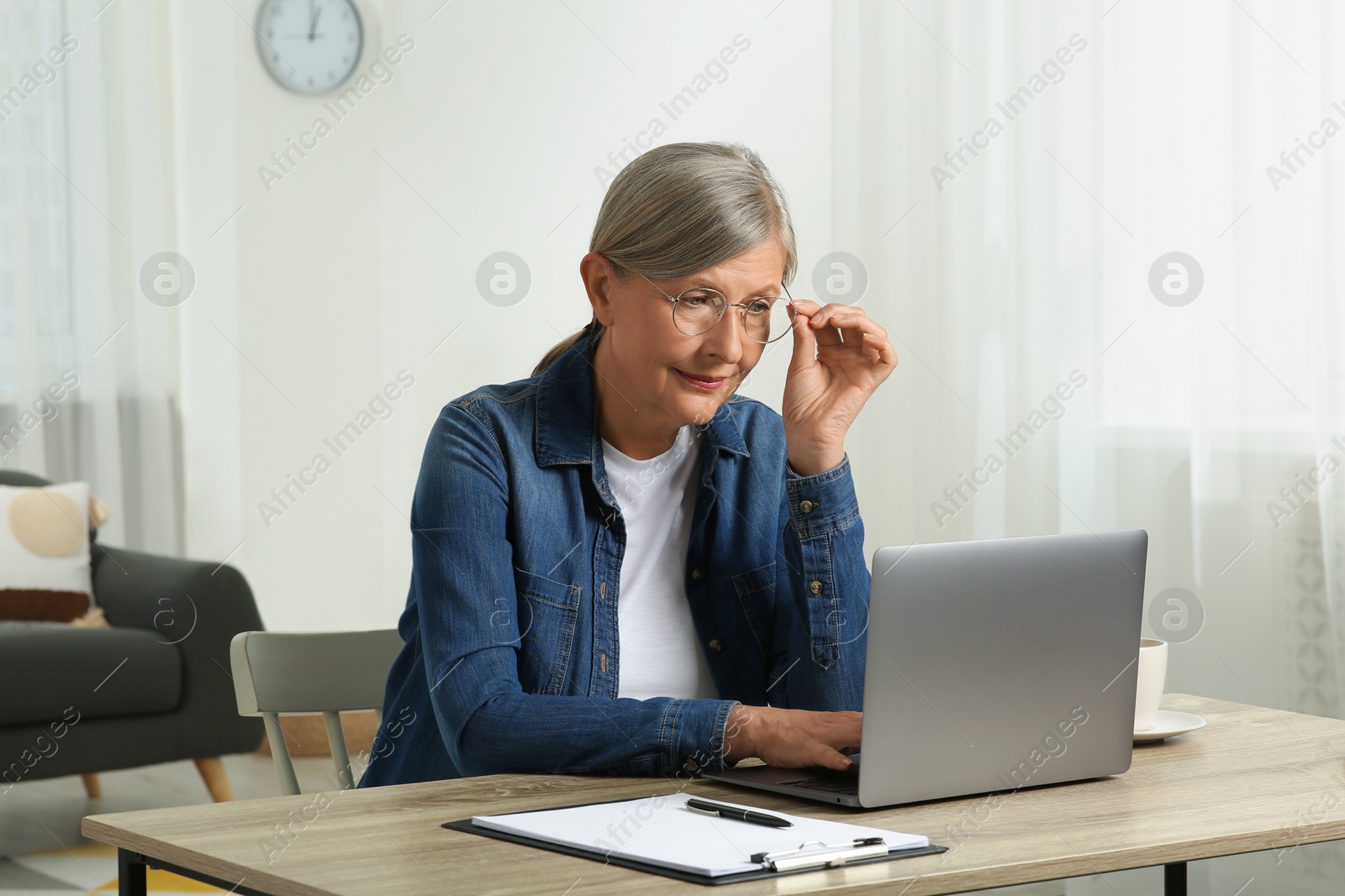 Photo of Beautiful senior woman using laptop at wooden table indoors