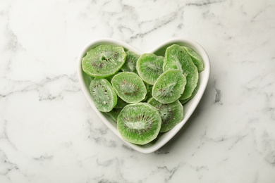 Photo of Bowl with slices of kiwi on marble background, top view. Dried fruit as healthy food