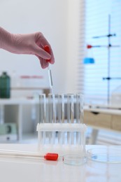 Photo of Laboratory analysis. Woman dripping liquid into test tubes at white table indoors, closeup