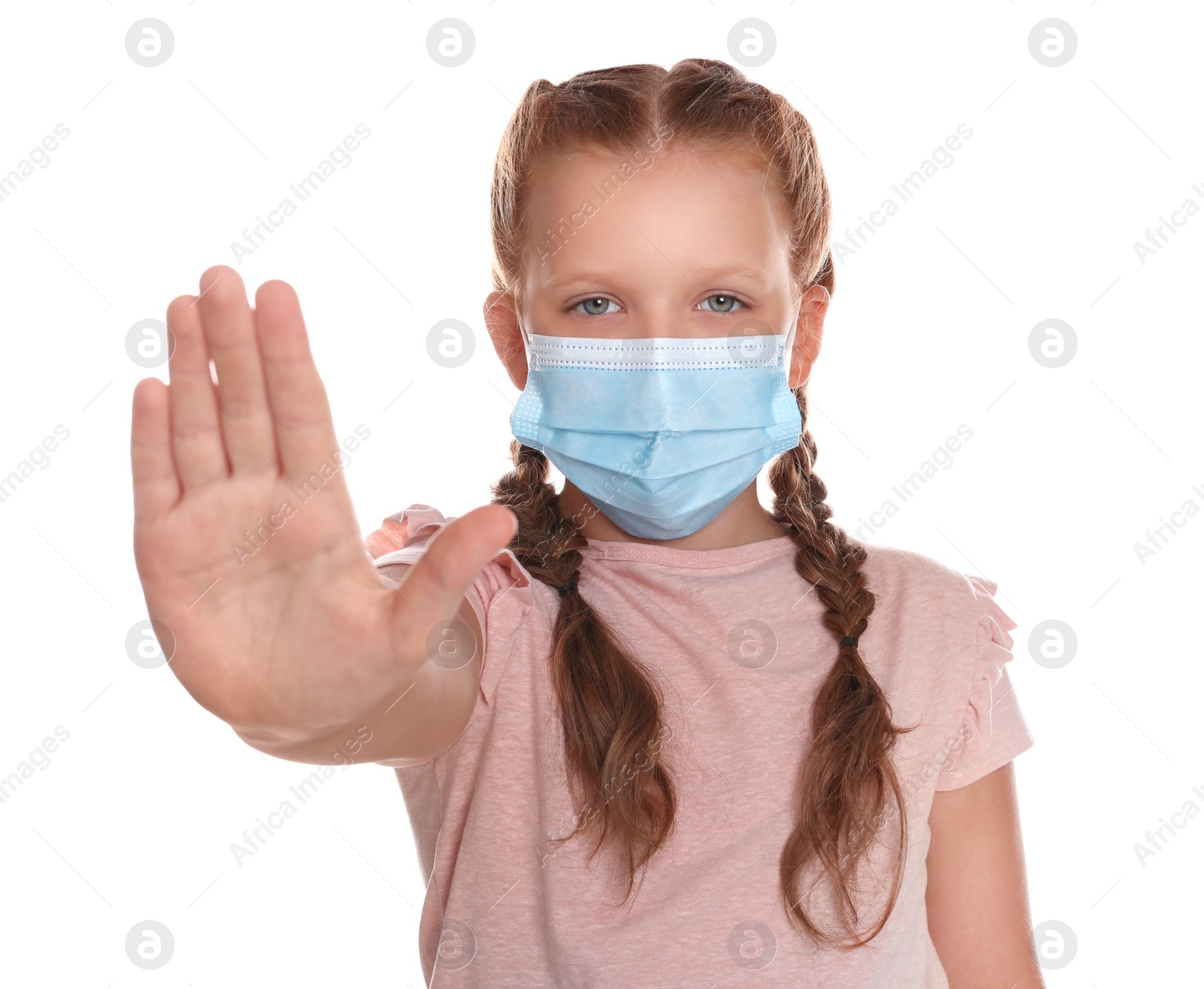 Photo of Little girl in protective mask showing stop gesture on white background. Prevent spreading of coronavirus