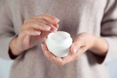 Photo of Young woman holding jar of cream on grey background, closeup