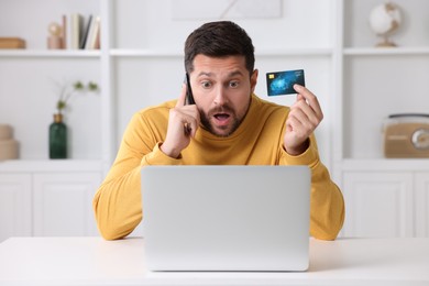 Photo of Scared man with credit card talking on smartphone near laptop at home. Be careful - fraud