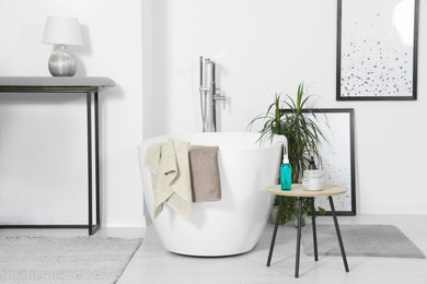 Photo of Stylish white tub and wooden table with toiletries in bathroom. Interior design