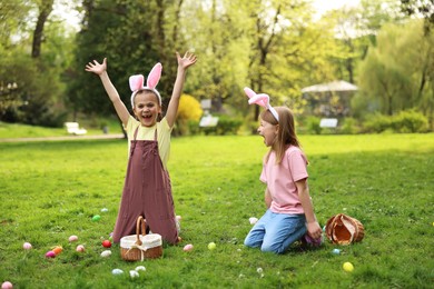 Photo of Easter celebration. Cute little girls in bunny ears hunting eggs outdoors