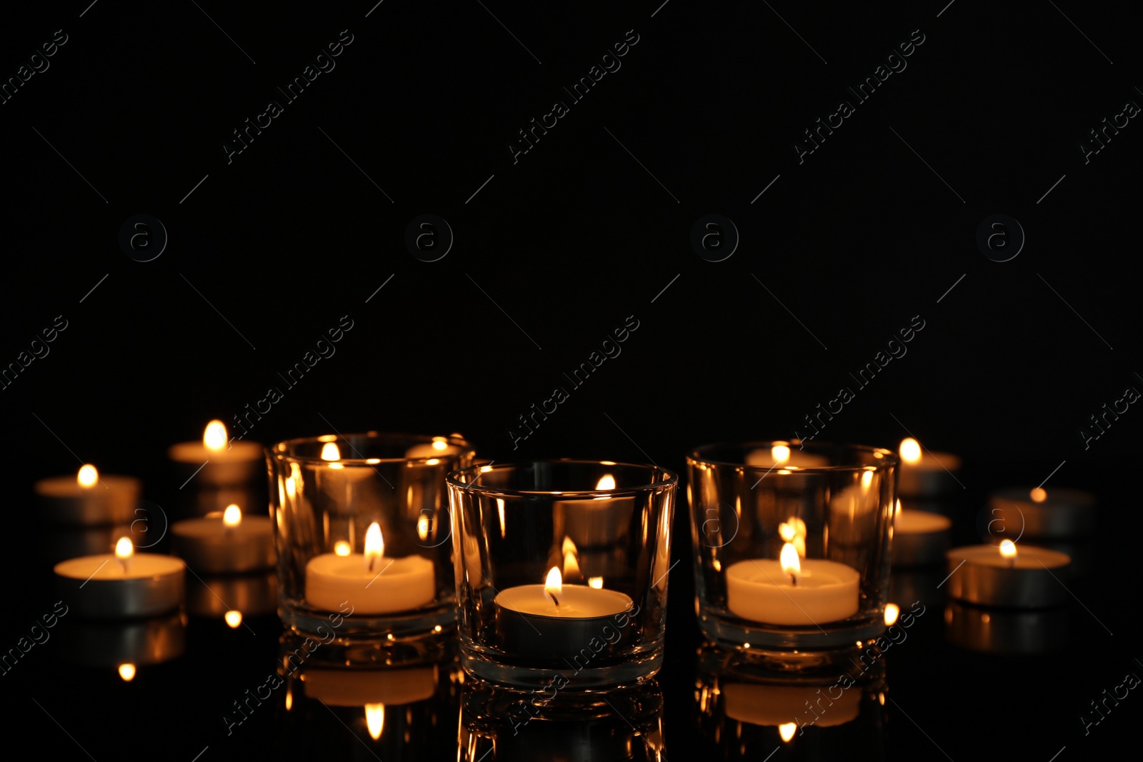 Photo of Burning candles in glass holders on table against dark background, space for text