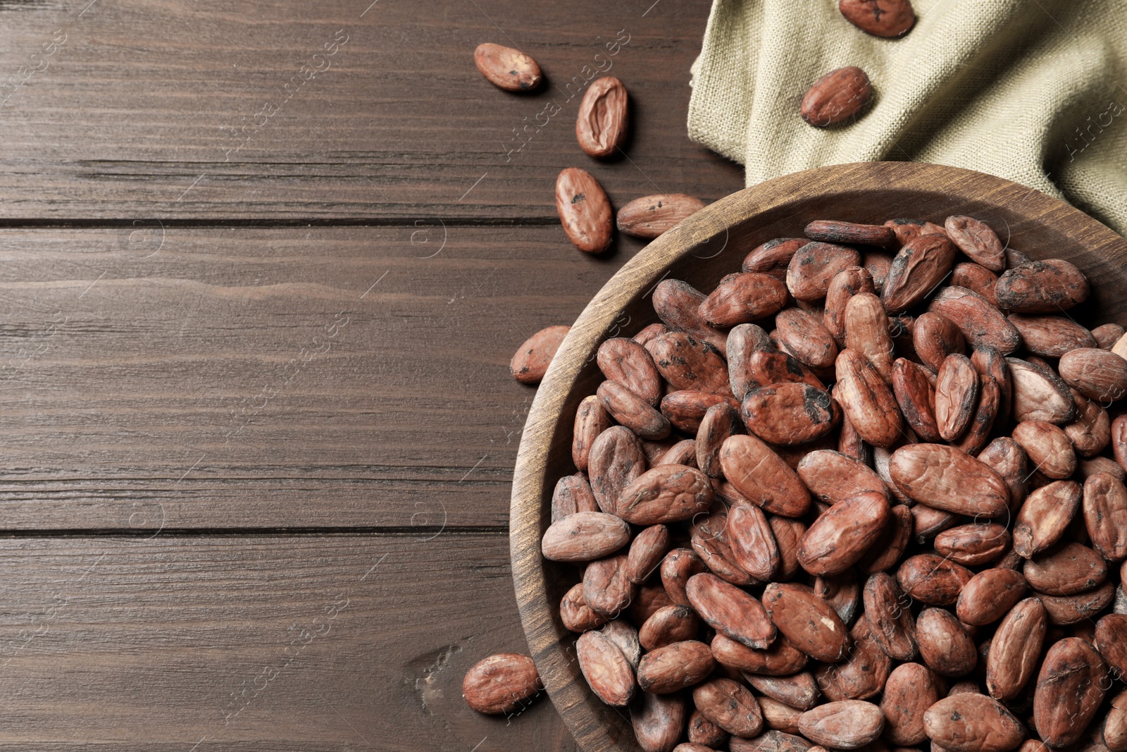 Photo of Bowl with cocoa beans on wooden table, top view. Space for text