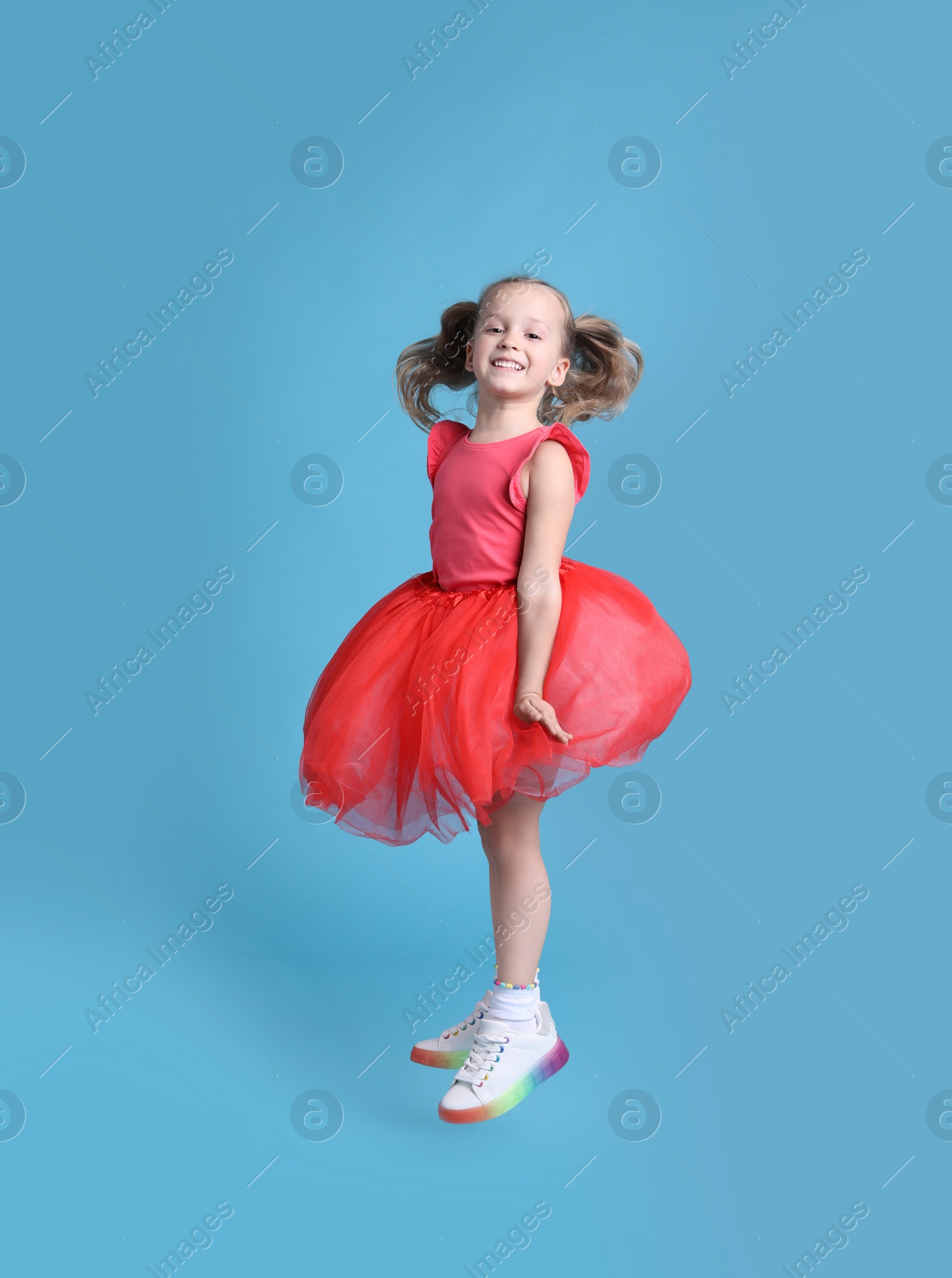 Photo of Cute little dancer in tutu skirt jumping on light blue background