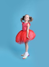 Photo of Cute little dancer in tutu skirt jumping on light blue background