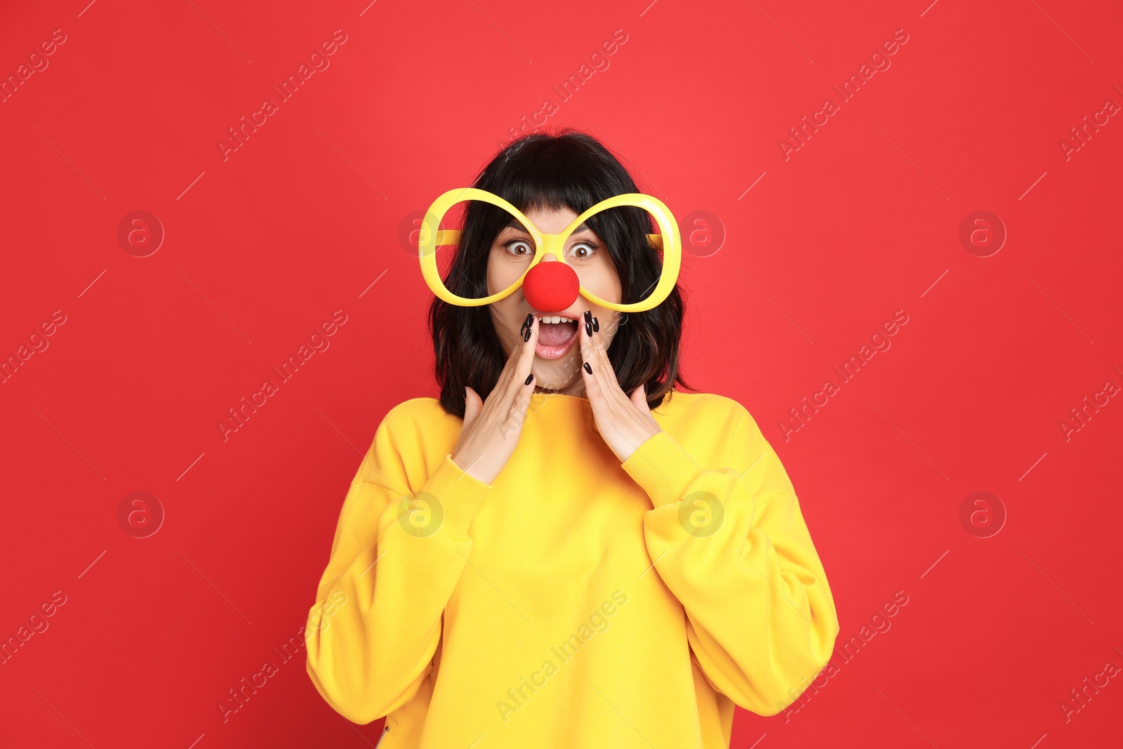 Photo of Emotional woman with large glasses and clown nose on red background. April fool's day