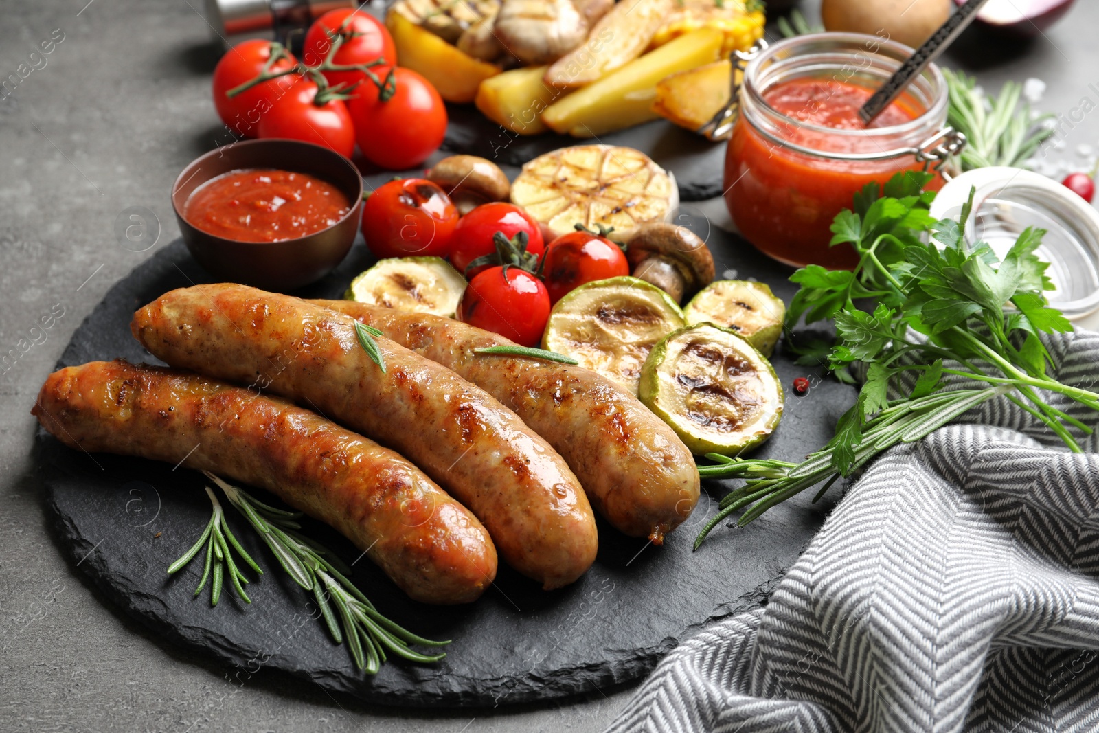 Photo of Slate plate with delicious sausages and vegetables served for barbecue party on gray table