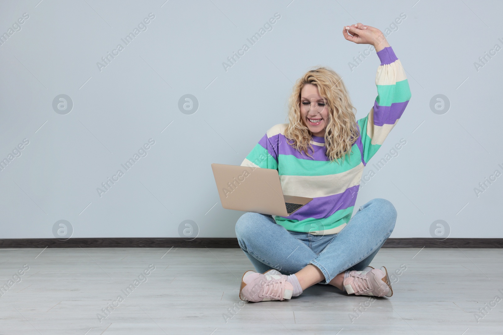 Photo of Beautiful young woman with laptop sitting on floor near grey wall. Space for text