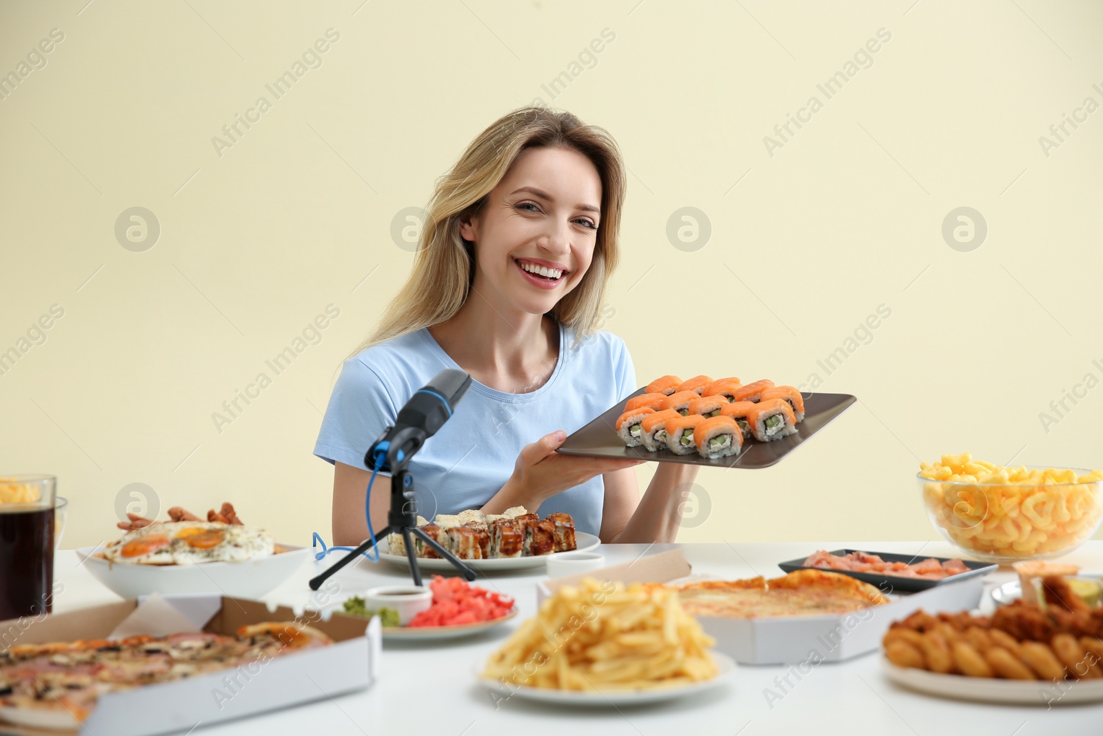 Photo of Food blogger eating in front of microphone at table against light background. Mukbang vlog