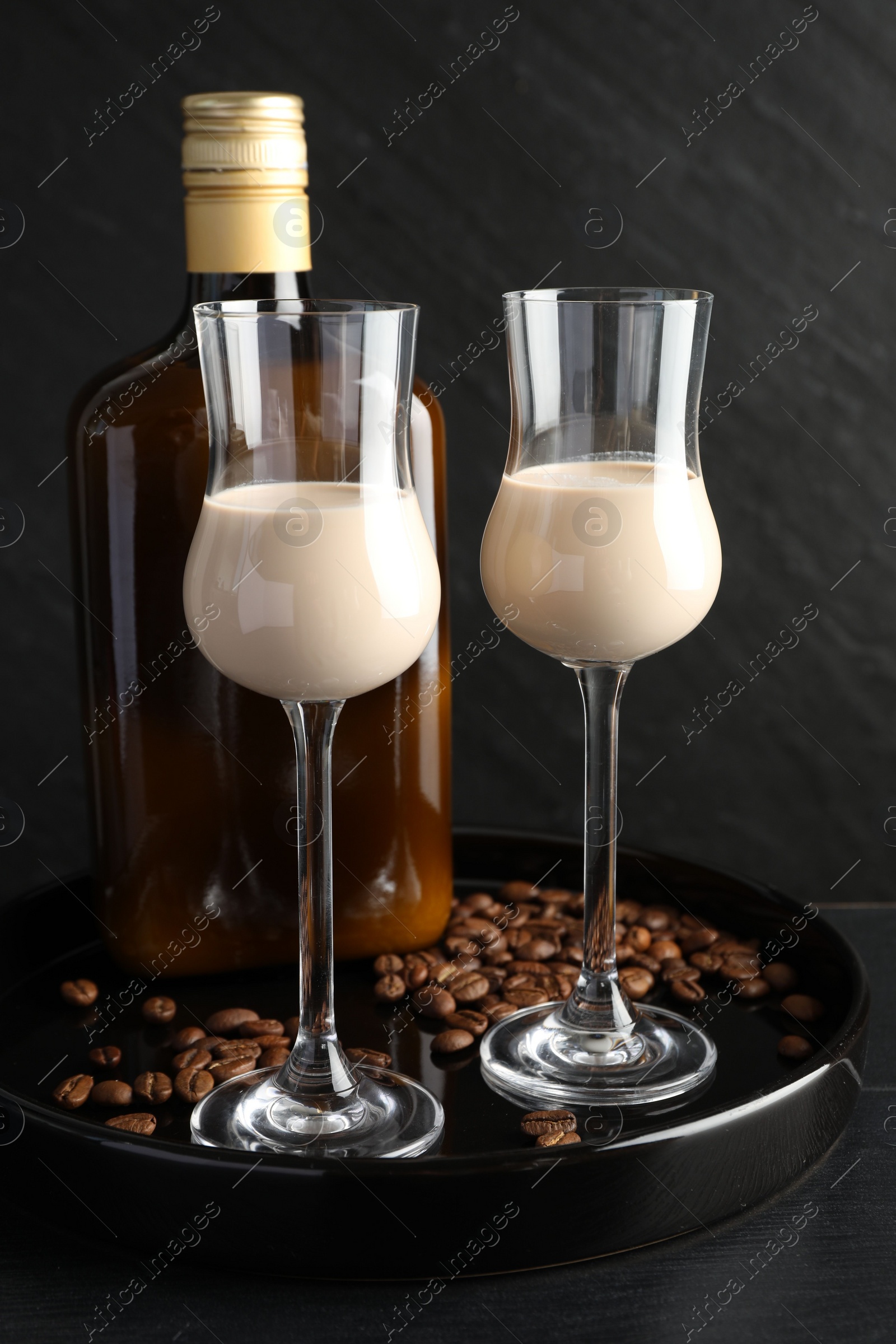 Photo of Coffee cream liqueur in glasses, bottle and beans on black wooden table