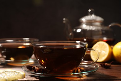 Photo of Aromatic tea with anise stars and lemon on wooden table, closeup