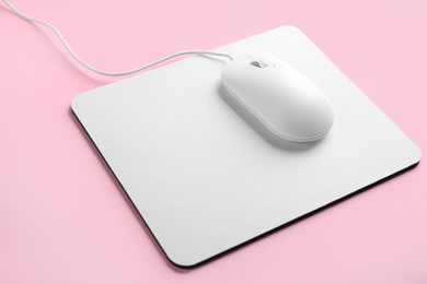 Photo of Modern wired optical mouse and pad on pink background