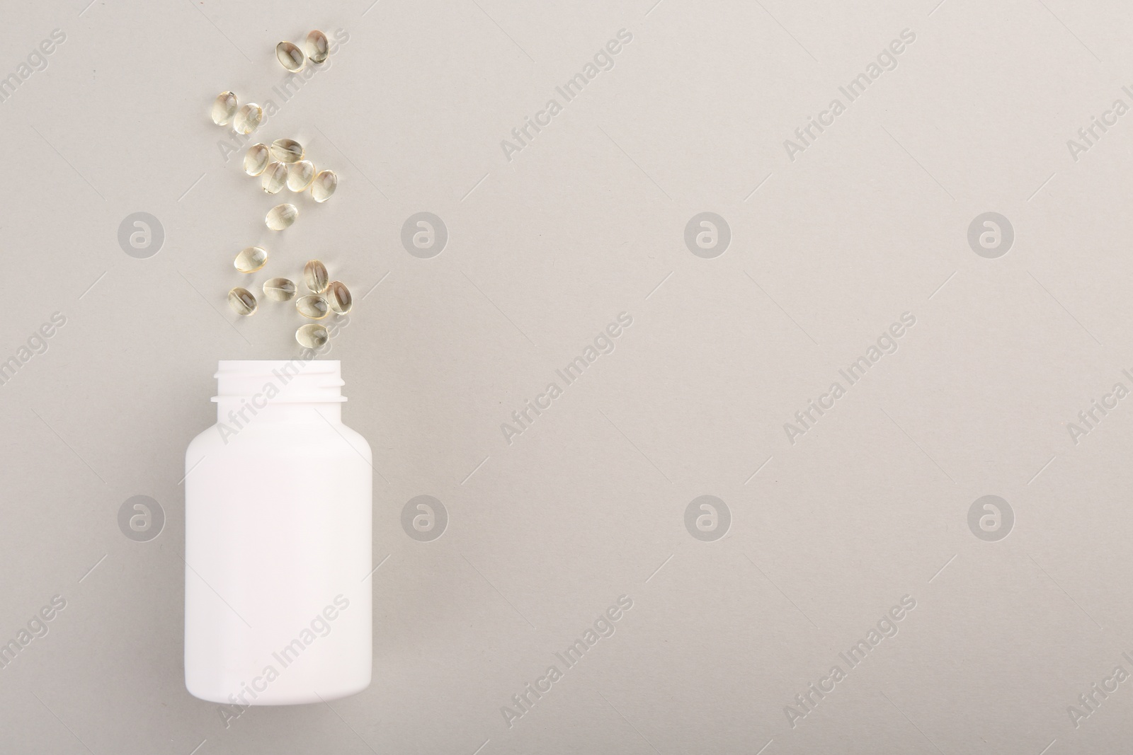 Photo of Bottle and vitamin capsules on light grey background, top view. Space for text