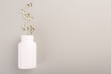 Photo of Bottle and vitamin capsules on light grey background, top view. Space for text