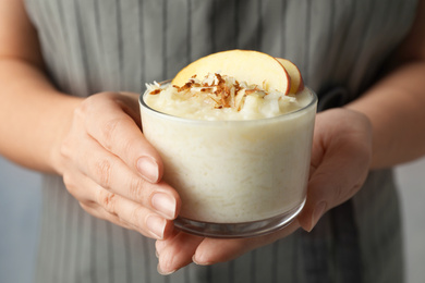 Photo of Woman holding glass of delicious rice pudding with apple and almond, closeup